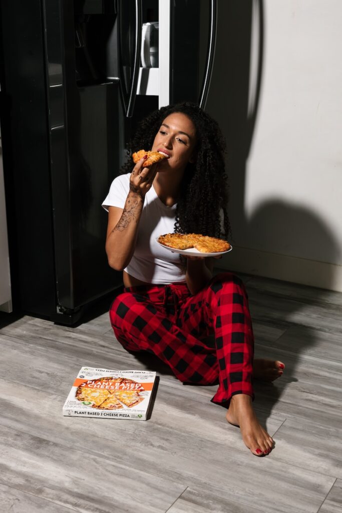 a woman sitting on the floor eating a piece of pizza